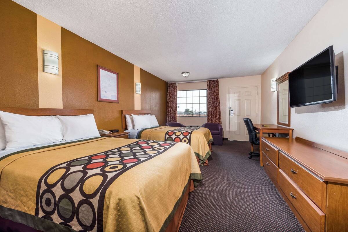 Habitación de hotel con dos camas, un escritorio, una silla, un televisor y una ventana con cortinas.