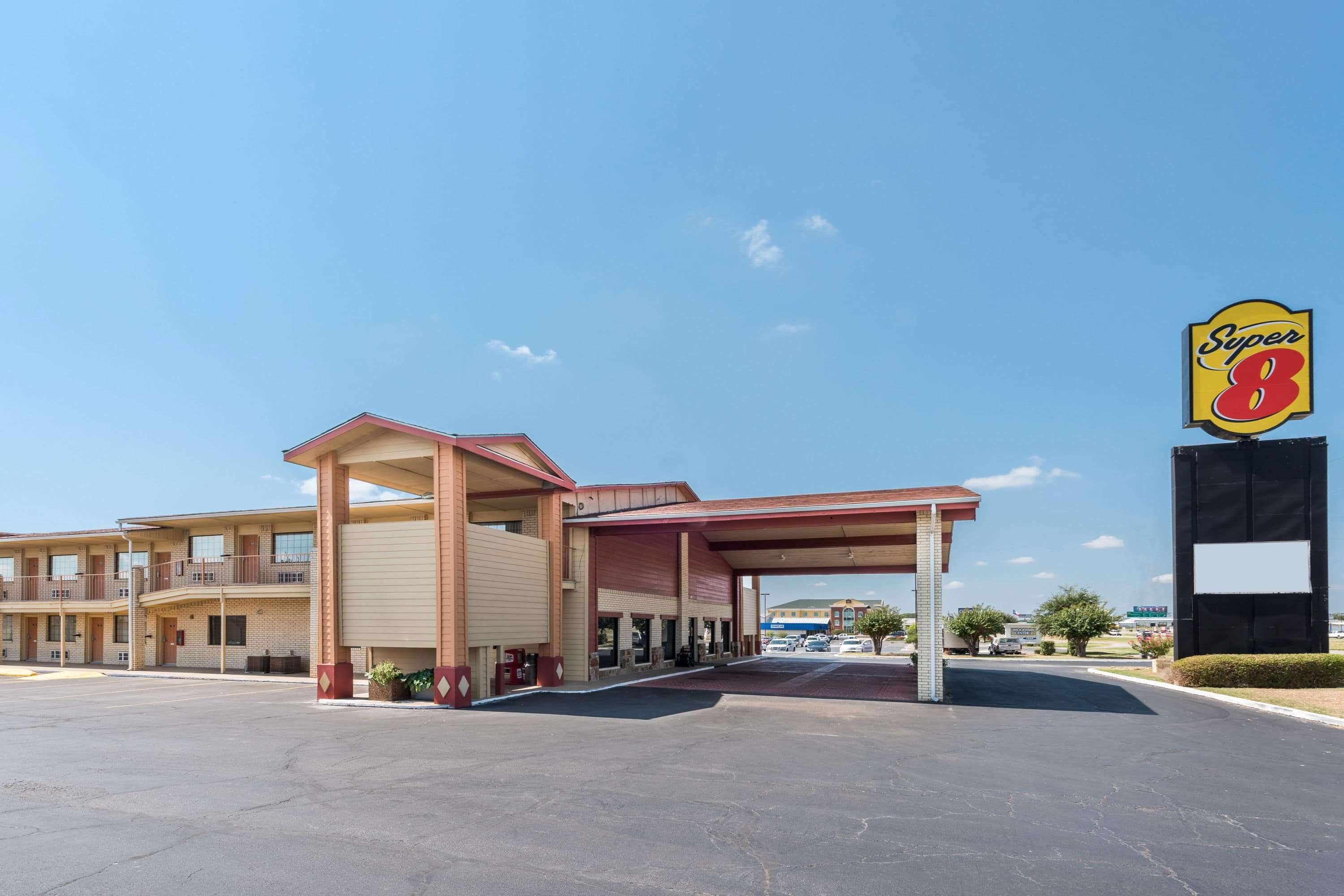 Un motel con letrero de Super 8, zona de estacionamiento techada y cielo despejado.