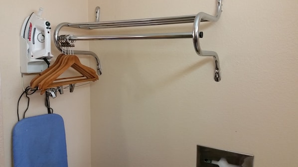 Un tablero de planchar fijado a la pared, una percha de madera y una silla azul.