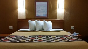 A hotel room with a large bed, a headboard, two wall-mounted lights, a framed picture, and a bedside table with a phone and a remote control.