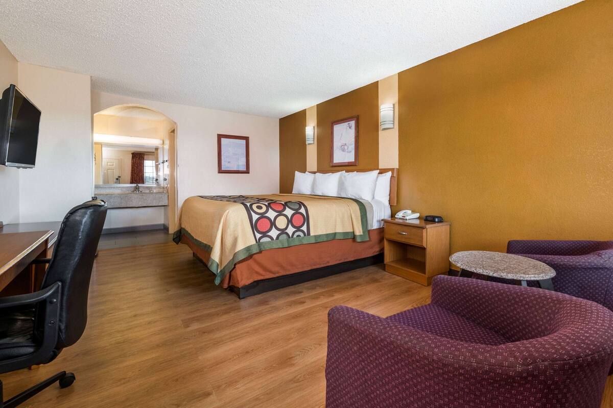 Habitación de hotel con cama, escritorio, silla, mesita y televisor.