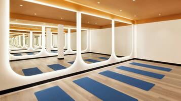 Una habitación amplia con suelo de madera, tapetes de yoga azules y un interior moderno, bien iluminado, con paredes y techo blancos.