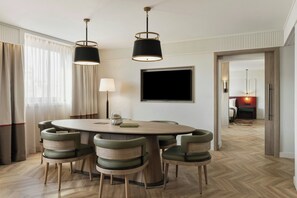 A dining area with a round table, six chairs, two pendant lights, a flat-screen TV, and a lamp.