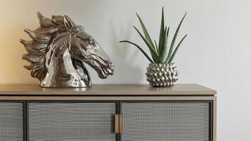 Une sculpture décorative représentant une tête de cheval et une plante en pot, posées sur un meuble en bois dont les portes sont faites d’un matériau tressé.