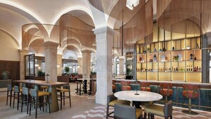 Un hall d’entrée spacieux avec un bar central, de hauts plafonds et un motif à carreaux sur le sol.