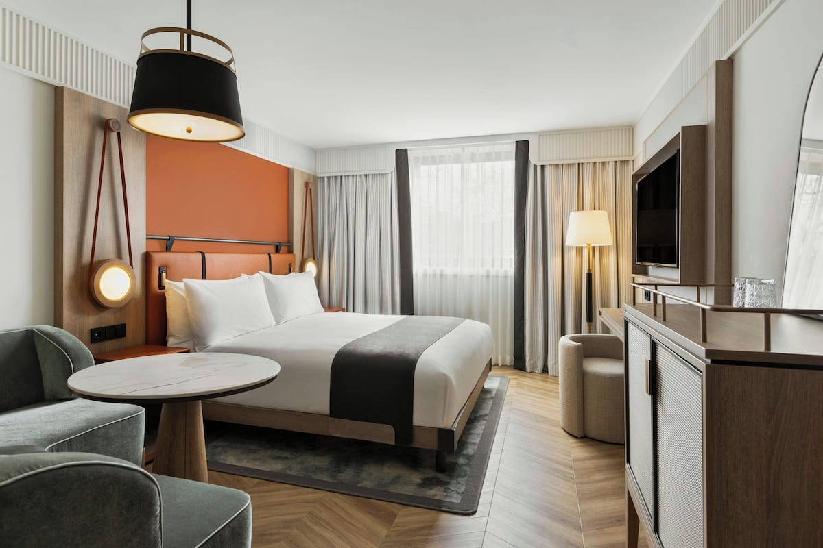 Una habitación de hotel moderna con una cama grande, una mesa redonda, un sofá, un televisor y un minibar.