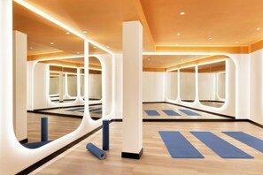 A spacious room with mirrored walls, wooden flooring, and yoga mats.