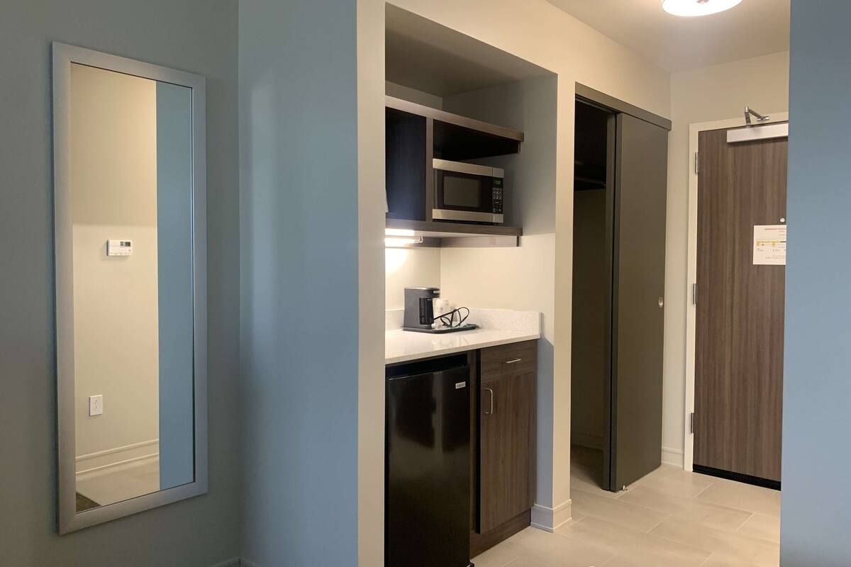 A modern kitchen with a microwave, coffee maker, and dishwasher. There is a large mirror on the wall and a door leading to another room.