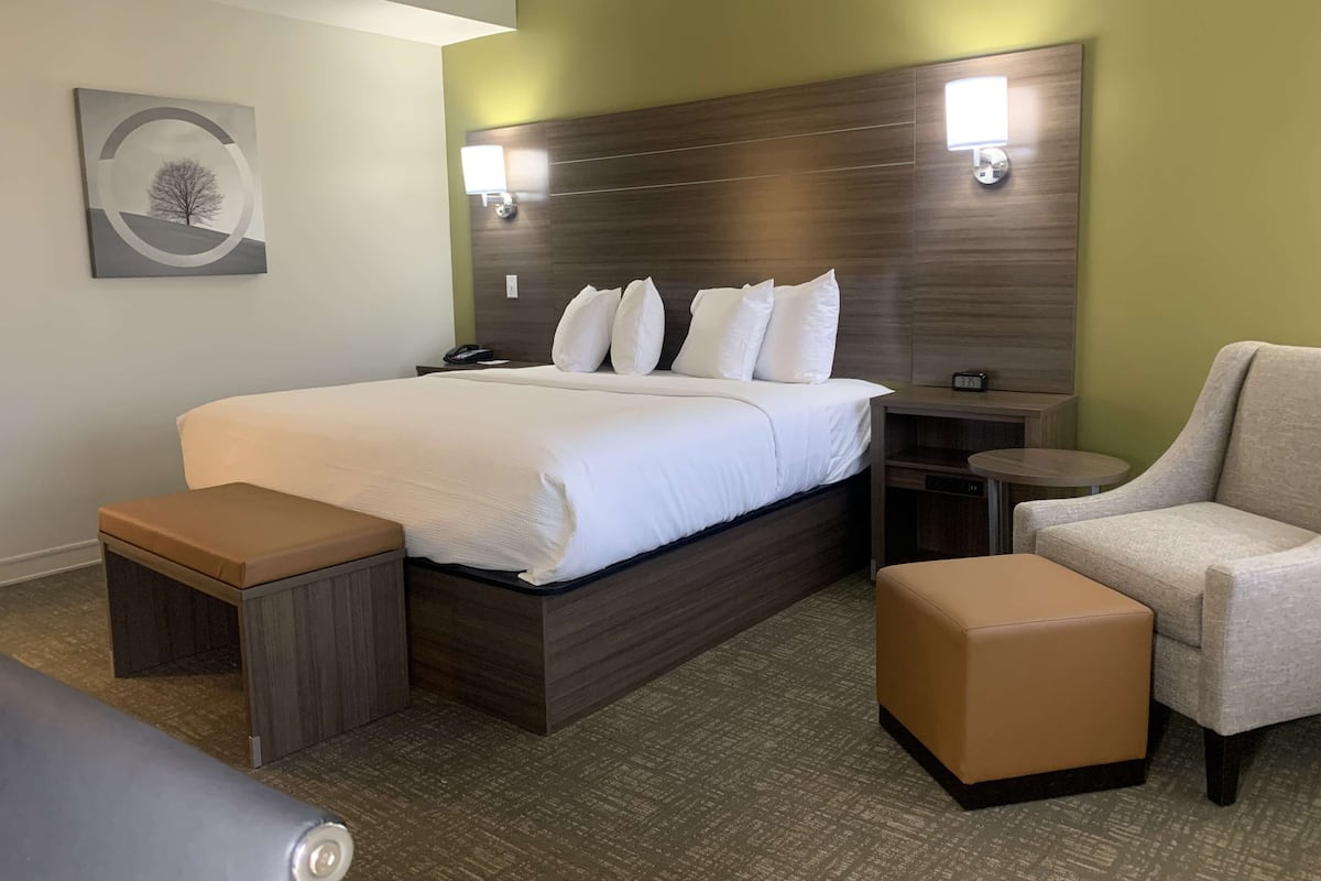 A hotel room with a large bed, bedside tables, a chair, and a small table.