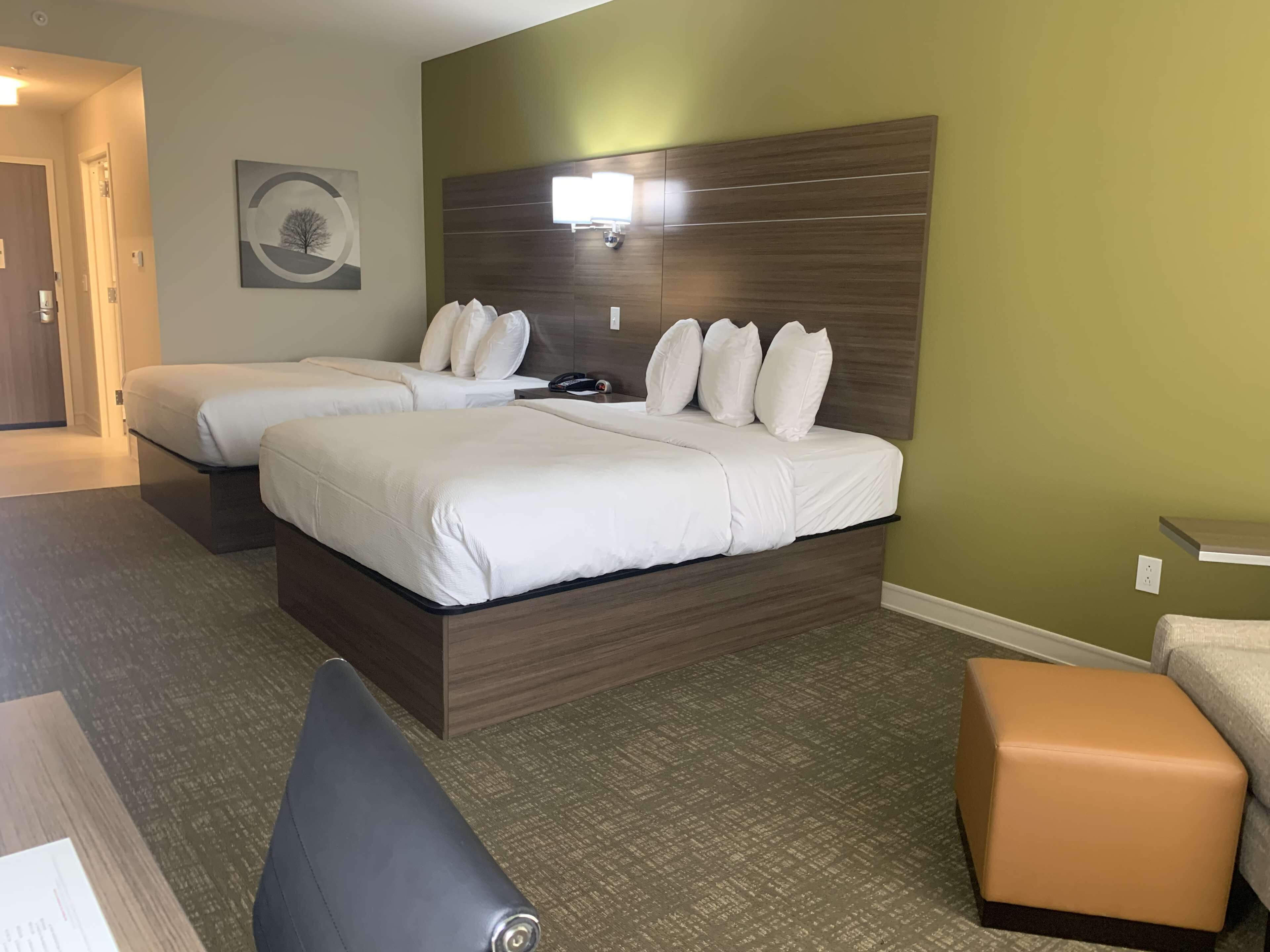 A hotel room with two beds, a desk, a chair, and a small ottoman.