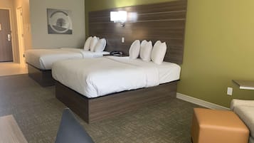 Ein Hotelzimmer mit zwei Betten, einem Schreibtisch, einem Sessel und einem kleinen Hocker.