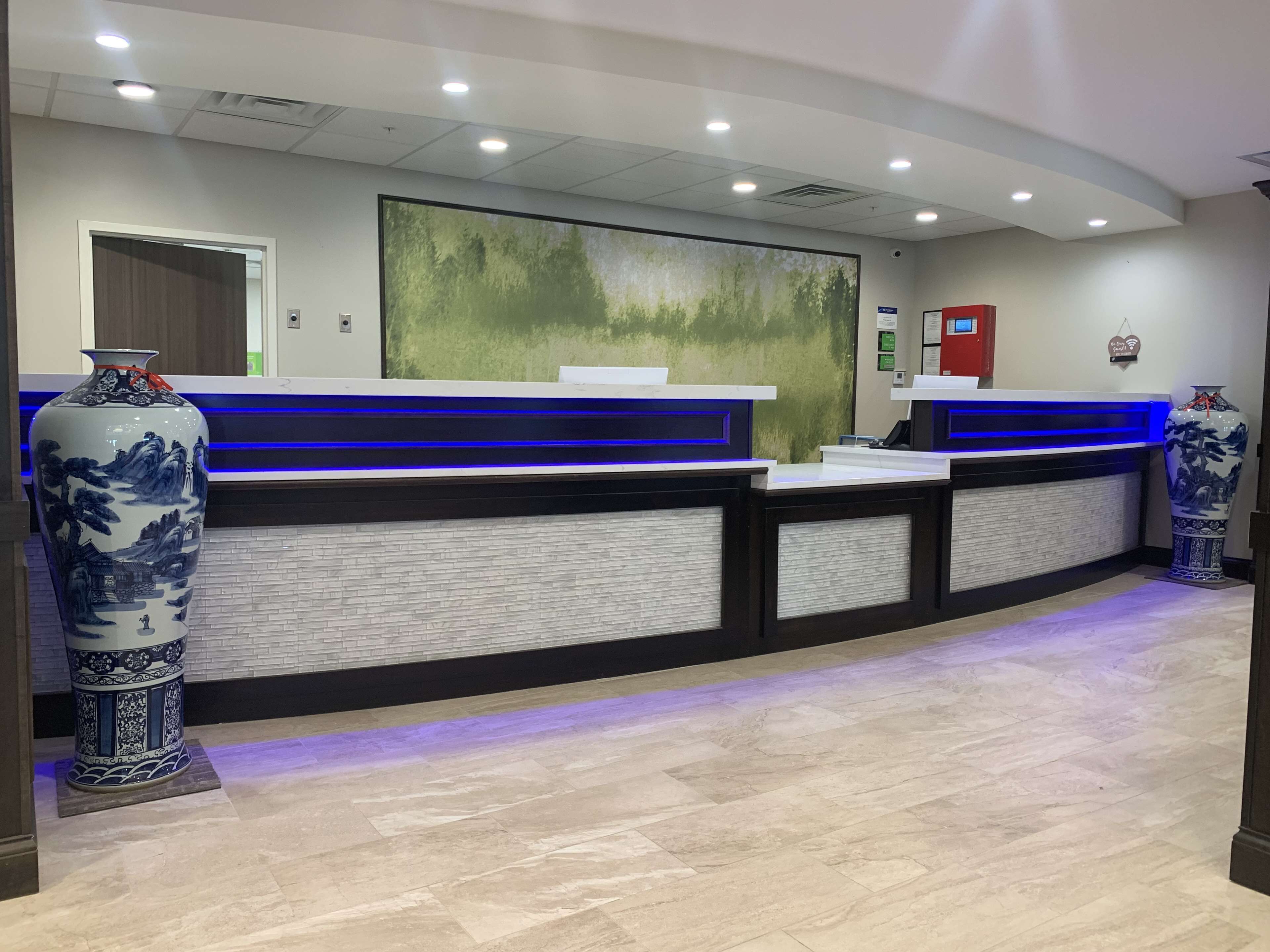 A reception area with a modern design, featuring a blue-lit reception desk, a large abstract painting on the wall, and traditional blue and white vases.