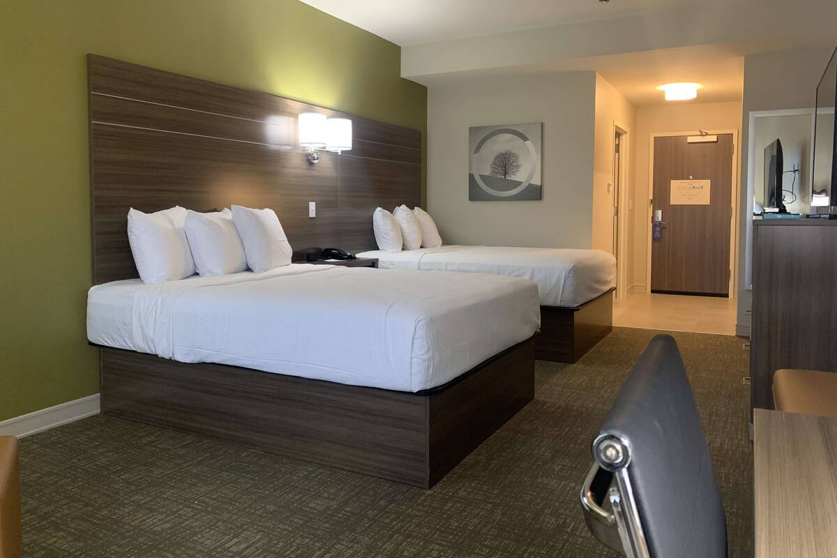 A hotel room with two beds, a desk, a chair, a desk lamp, a telephone, and a painting on the wall.