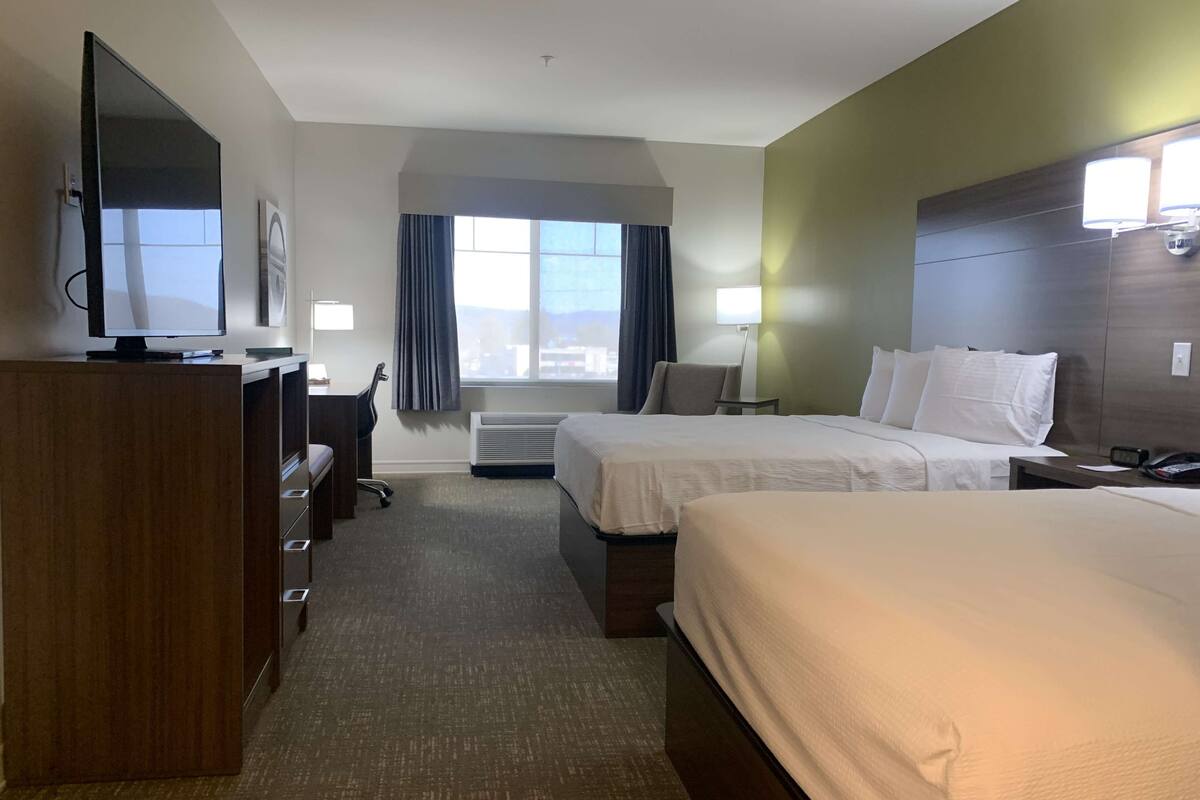 A hotel room with two beds, a desk with a chair, a television, and a window with curtains.
