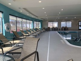 Un área de piscina con sillones reclinables y mesas, amplias ventanas y vistas despejadas al exterior.