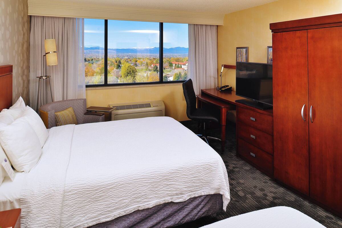 Habitación de hotel con una cama grande, un escritorio con televisor, un armario y vistas al paisaje por la ventana.