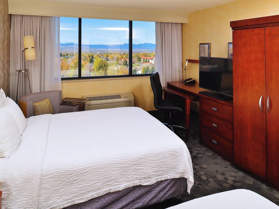 Ein Hotelzimmer mit einem großen Bett, einem Schreibtisch mit Fernseher, einem Kleiderschrank und Blick auf eine Landschaft durch das Fenster.