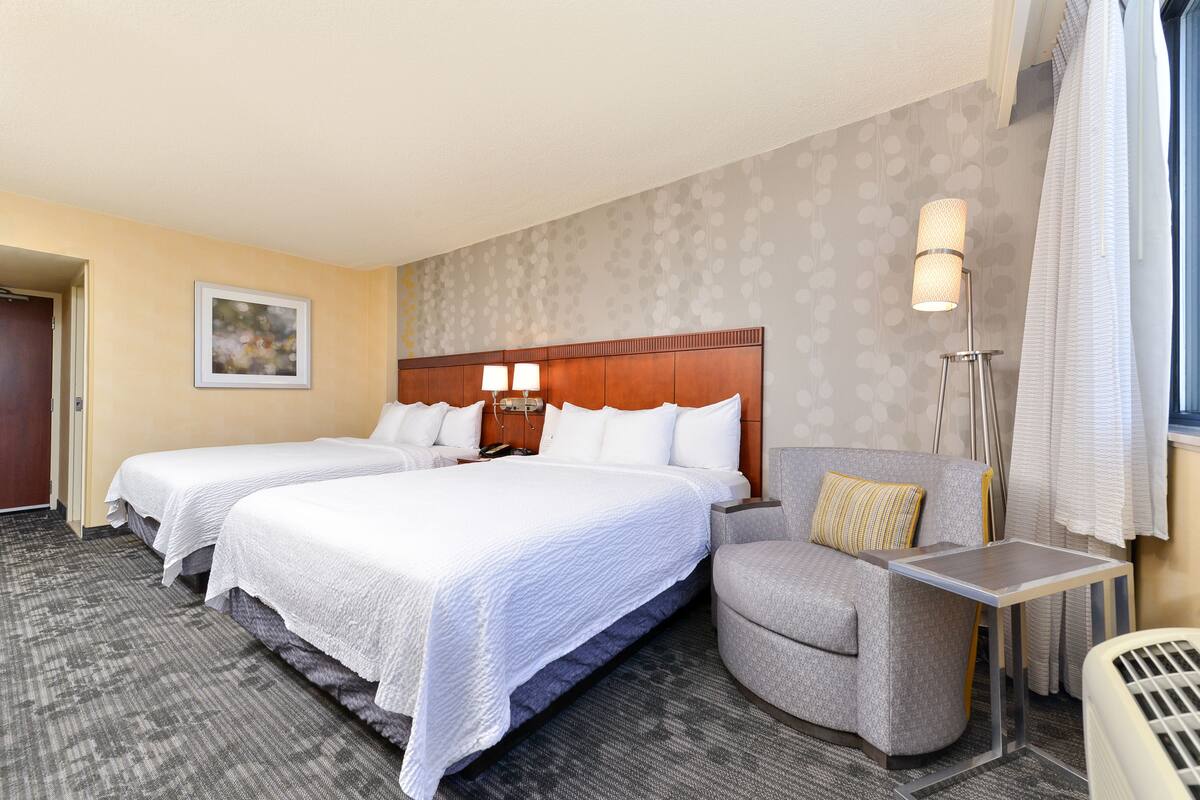 Una habitación de hotel con dos camas, un sofá, una mesita y una lámpara de pie.