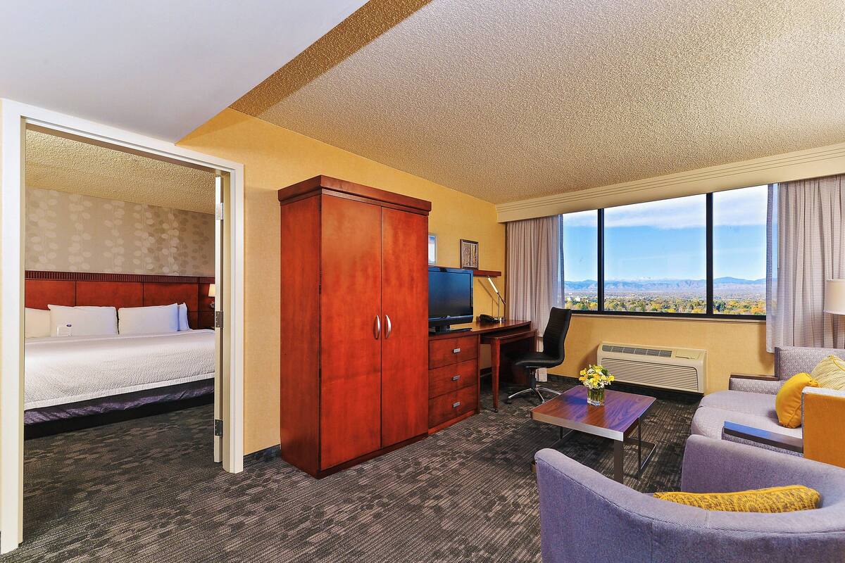 Habitación de hotel con cama, escritorio, sillón, sofá y vista a la ciudad.