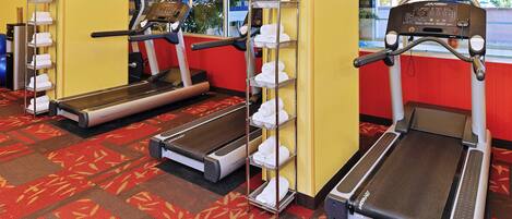 A gym with treadmills, a wall-mounted TV, and a towel rack.