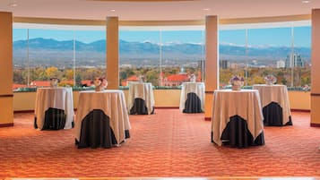 Habitación de hotel con vistas panorámicas a la montaña, varias mesas con manteles blancos y una alfombra roja estampada.