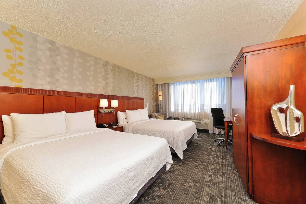 Habitación de hotel con dos camas, un escritorio, una silla y un armario.