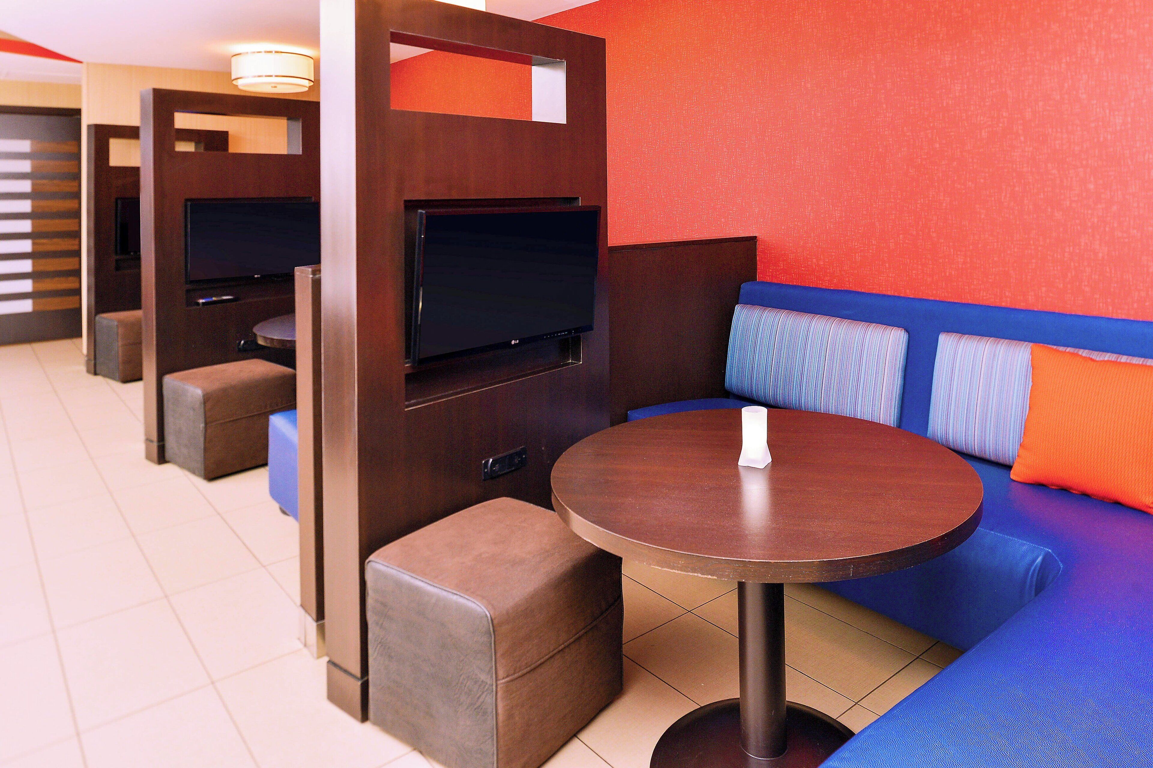 Un área de descanso moderna con una mesa redonda, asientos acolchados y un televisor de pantalla plana integrado en un panel de madera.
