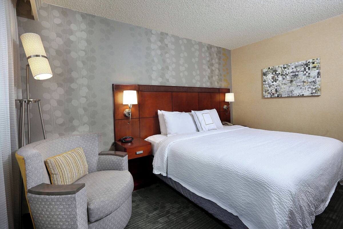 Habitación de hotel con una cama grande, una mesita de noche, una silla y una pared con textura.