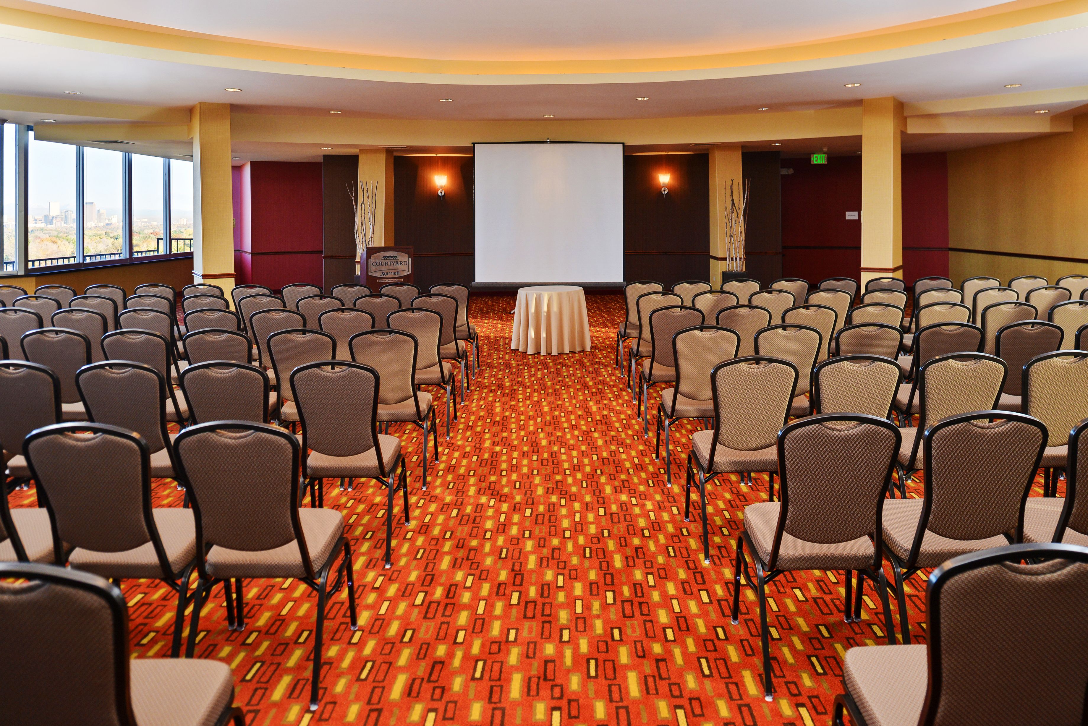 A conference room with rows of chairs, a carpeted floor, a projection screen, and a table.