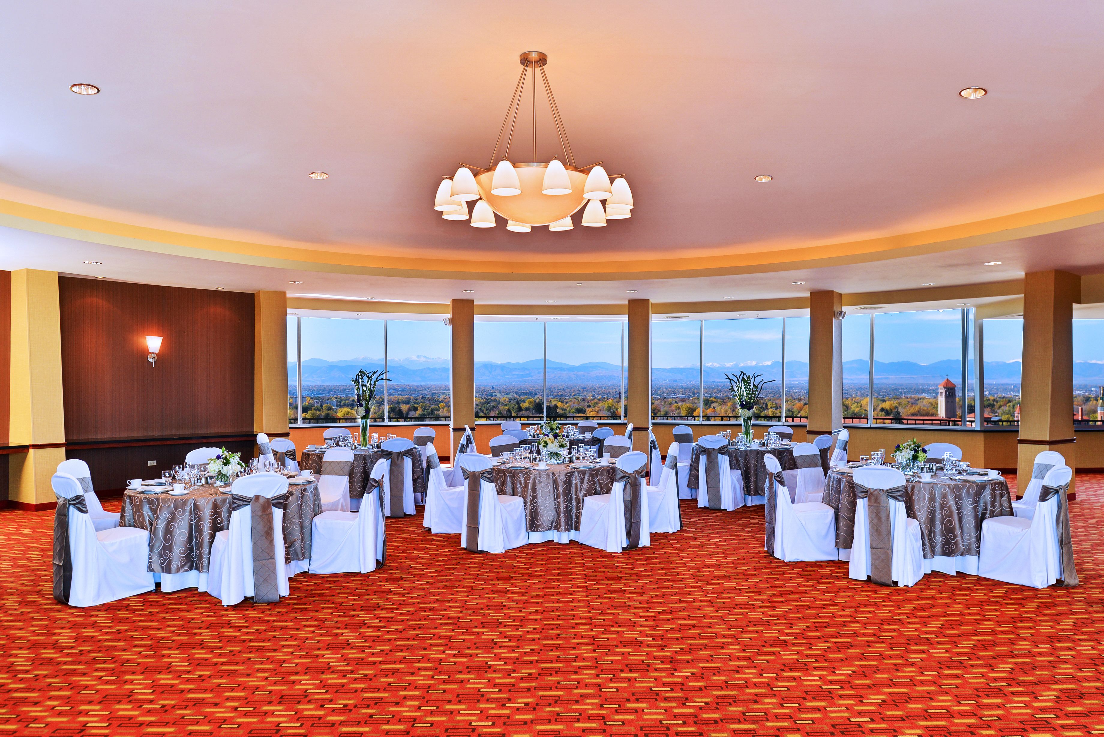 Une salle de banquet avec des tables rondes, des chaises blanches et grises, et un grand lustre.