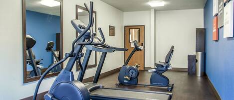 Un gimnasio con cintas de correr y elípticas, un espejo y una puerta que da a otra habitación.
