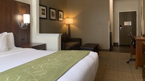 Una habitación de hotel con cama, escritorio, silla, lámpara y puerta.