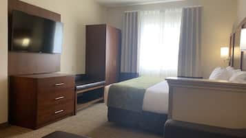 A hotel room with a bed, a TV mounted on the wall, a wardrobe, a desk, and a window with curtains.