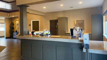 A hotel reception area with a counter, a digital screen, and a hand sanitizer dispenser.