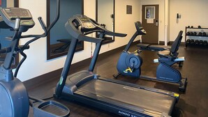 Un gimnasio con cintas de correr, elípticas y un estante de mancuernas.