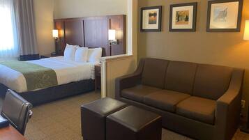 A hotel room with a large bed, a sofa, an ottoman, a desk, and two framed pictures on the wall.