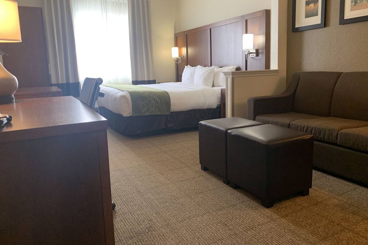 A hotel room with a bed, two bedside tables, a desk, a sofa, and two ottomans.