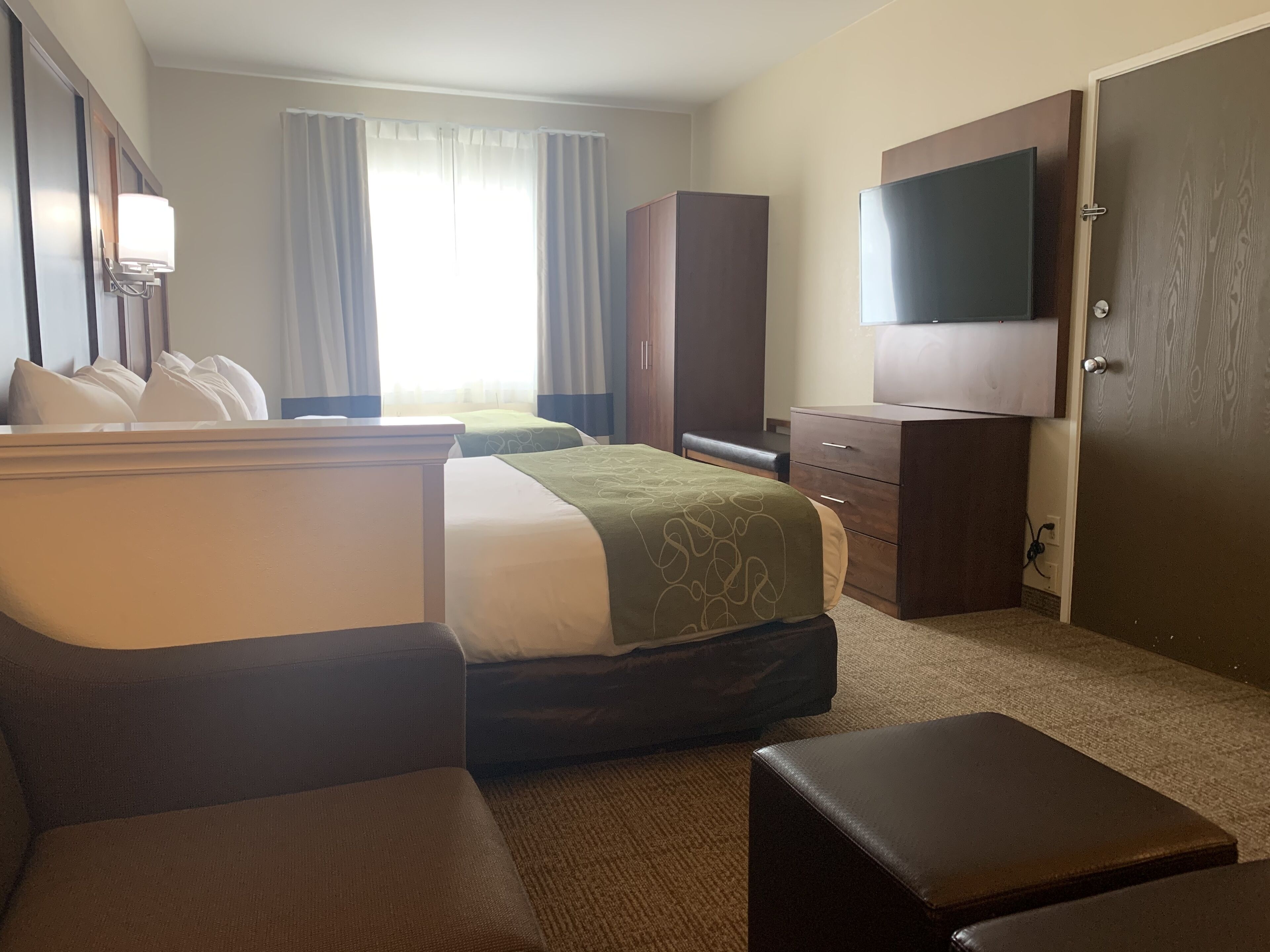 Ein Hotelzimmer mit Bett, Schreibtisch, Stuhl, Kommode, Fernseher und einer Tür.