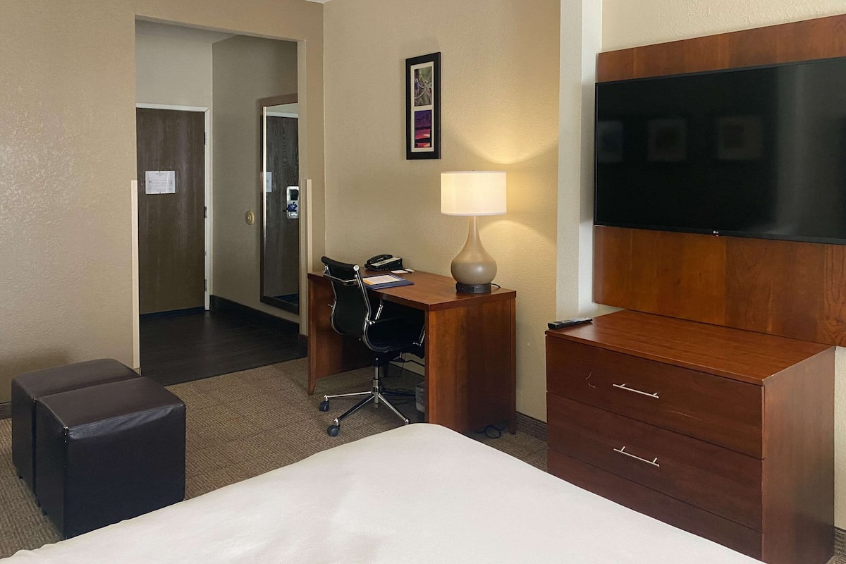 Ein Hotelzimmer mit Bett, Schreibtisch mit Stuhl, Lampe, Fernseher und einem Holzschrank.