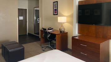 Habitación de hotel con cama, escritorio con silla, lámpara, televisor y cómoda de madera.