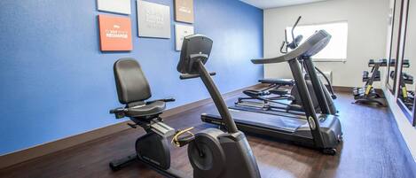A gym with exercise equipment, including stationary bikes and treadmills, against a blue wall with motivational posters.