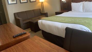 Una habitación de hotel con cama, sofá, escritorio, lámpara y cuadros en la pared.