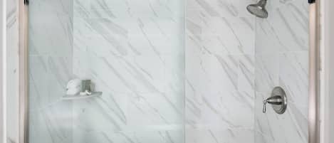 A modern bathroom with a glass-enclosed shower, marble tiles, and a towel rack.