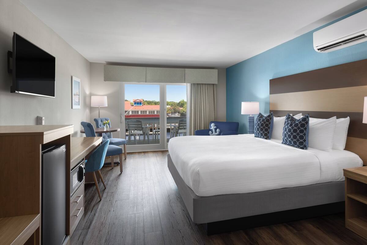 A hotel room with a bed, desk, and chair, a TV, and an air conditioning unit.