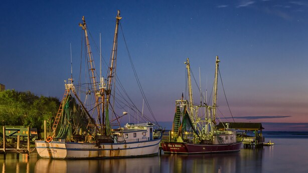Two fishing boats docked at a pier with calm water and a clear sky. - Shem Creek Inn (Mount Pleasant)