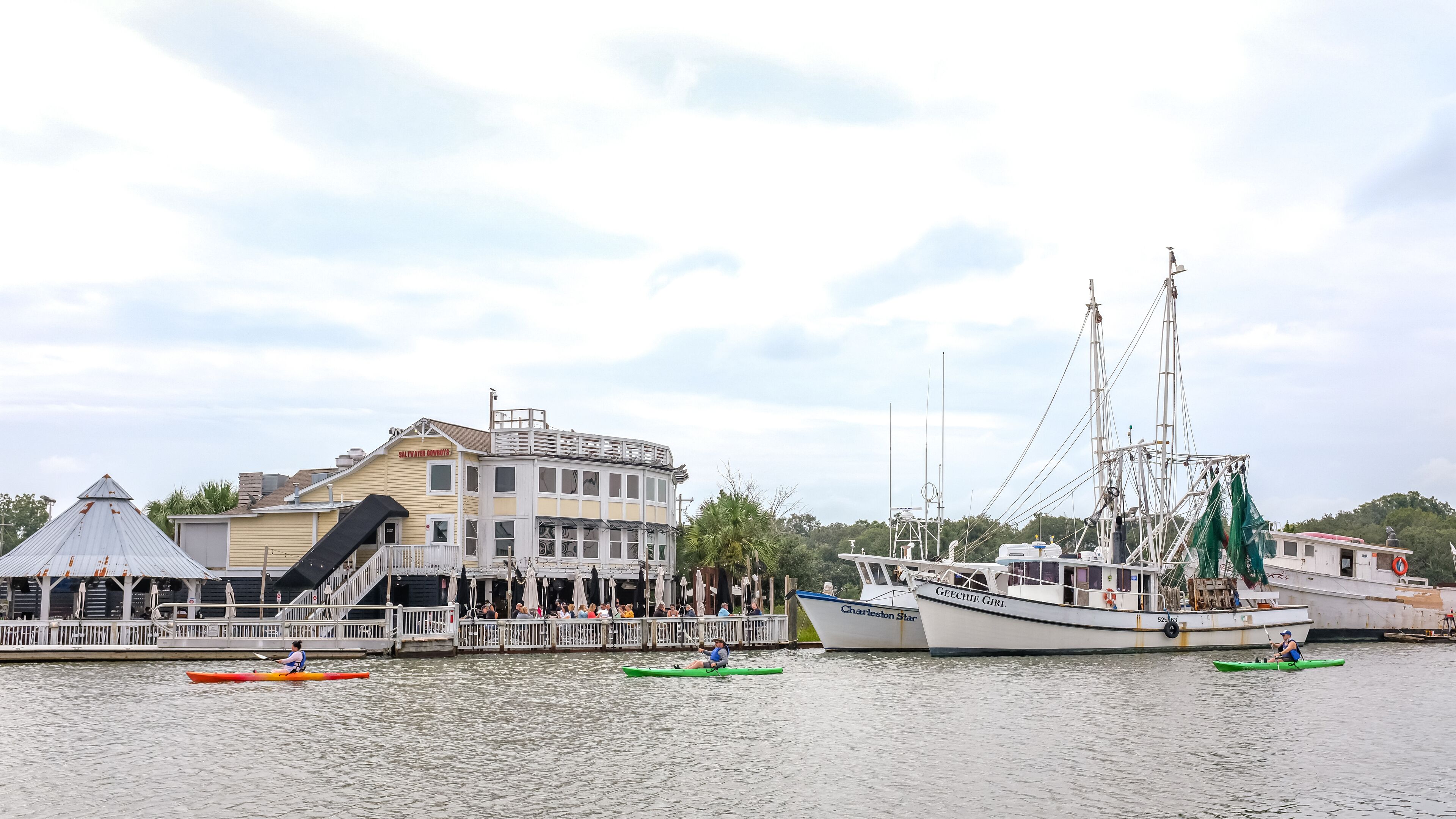 Un edificio frente al agua con un muelle, un velero grande y varias kayaks.
