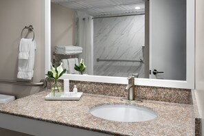 A bathroom with a granite countertop, a white sink, a mirror, and a shower area with a glass door.