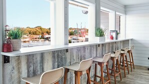 A bar area with wooden stools and a white counter, overlooking a dock and boats. - Shem Creek Inn (Mount Pleasant)