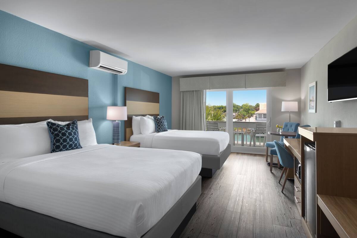 A hotel room with two beds, a desk, and a balcony with a view.