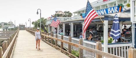 Une promenade en bois abritant un restaurant appelé « Bana Bar », doté d’une terrasse et décoré de drapeaux américains.